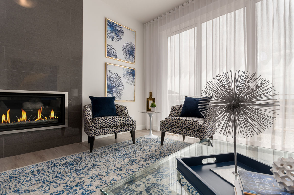 Living room with large grey tile fire place and two matching white and plack diamond print chairs in the Wilshire model home.