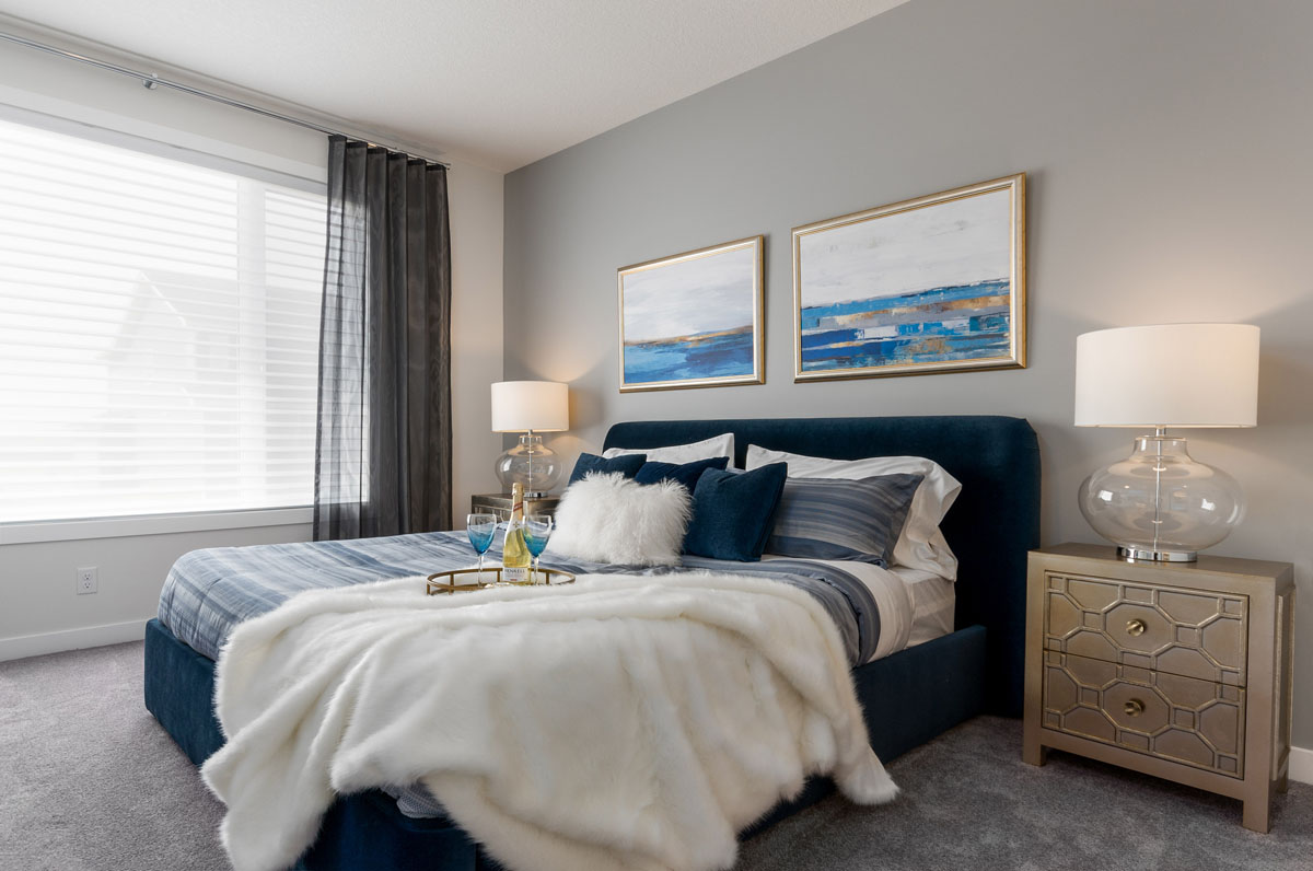 Facing the king size bed in the Wilshire model home with wine glasses and try on the bed.
